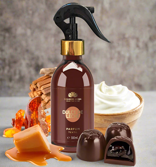 Brown spray bottle with gold cap labeled 'Dulce de Leche' surrounded by caramel, chocolate, and whipped cream on a light background.